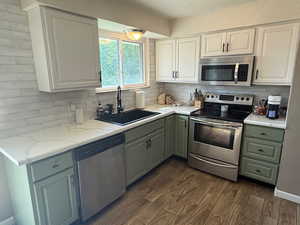 Kitchen featuring stainless steel appliances, a sink, tasteful backsplash, dark wood finished floors, and white cabinets