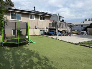 Back of house featuring a trampoline, a lawn, and roof mounted solar panels
