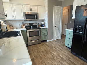 Kitchen with stainless steel appliances, a sink, decorative backsplash, white cabinetry, and light wood-type flooring