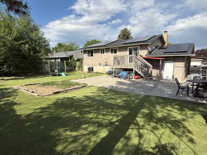 Back of house featuring a patio area, a trampoline, roof mounted solar panels, and a chimney