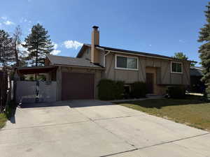 Raised ranch featuring a chimney, a garage, concrete driveway, stucco siding, and a gate