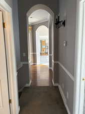 Hallway with ornamental molding, dark colored carpet, and arched walkways