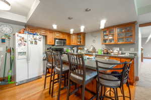Kitchen with white refrigerator with ice dispenser, brown cabinetry, black electric range oven, and a breakfast bar area