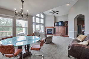 Dining area featuring a chandelier, carpet, a tiled fireplace, arched walkways, and ceiling fan