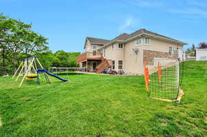 Rear view of property with stucco siding, stone siding, a wooden deck, stairs, and a playground