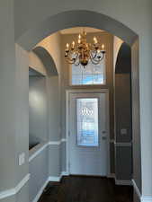 Foyer entrance with arched walkways, dark wood-style flooring, a chandelier, and a towering ceiling