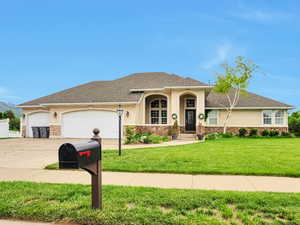 View of front of property with concrete driveway, stucco siding, a front lawn, a garage, and stone siding