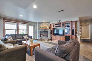 Living area with a stone fireplace, recessed lighting, and light colored carpet