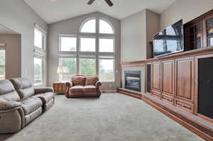 Carpeted living area with ceiling fan, high vaulted ceiling, and a fireplace