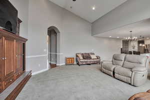 Living room with high vaulted ceiling, carpet flooring, a chandelier, arched walkways, and baseboards