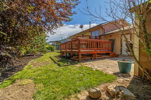 View of green lawn with a wooden deck and a patio area