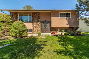 Bi-level home with stone siding, stucco siding, and a front lawn