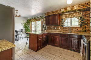 Kitchen featuring a sink, a textured ceiling, a peninsula, healthy amount of natural light, and light stone countertops