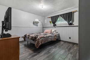 Bedroom with a textured ceiling, dark wood-style flooring, wainscoting, and wood walls