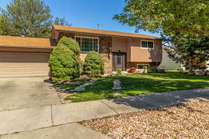 Raised ranch featuring stone siding, a front yard, stucco siding, and driveway