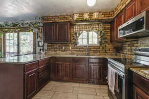 Kitchen with appliances with stainless steel finishes, a sink, a textured ceiling, a peninsula, and light stone countertops