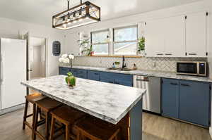 Kitchen featuring stainless steel appliances, a sink, blue cabinetry, light wood-type flooring, and decorative backsplash