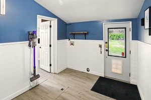 Entryway with vaulted ceiling, a wainscoted wall, wood finished floors, and wood walls