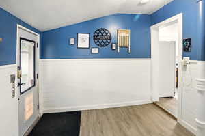 Doorway to outside with lofted ceiling, a wainscoted wall, wood finished floors, and a textured ceiling