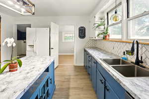 Kitchen with blue cabinets, white fridge with ice dispenser, a sink, and decorative backsplash