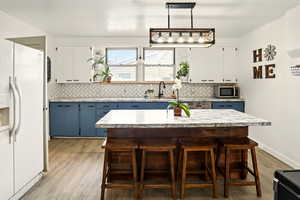 Kitchen with white fridge with ice dispenser, stainless steel microwave, blue cabinetry, a sink, and light countertops