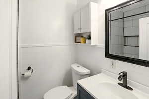 Bathroom with toilet, vanity, tile walls, and a wainscoted wall