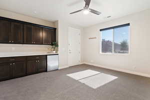 Kitchen featuring fridge, baseboards, carpet, a ceiling fan, and dark brown cabinets