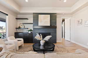 Living room with light wood-style flooring, baseboards, a tiled fireplace, recessed lighting, and a raised ceiling