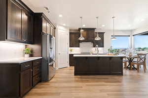 Kitchen featuring stainless steel refrigerator with ice dispenser, a breakfast bar, light countertops, light wood-style floors, and recessed lighting