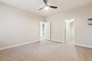 Unfurnished bedroom with light carpet, baseboards, ensuite bath, and ceiling fan