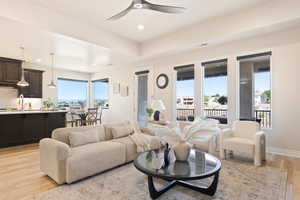 Living area with recessed lighting, light wood-type flooring, a ceiling fan, baseboards, and a tray ceiling
