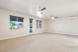 Empty room featuring healthy amount of natural light, light colored carpet, a wall mounted AC, and a ceiling fan