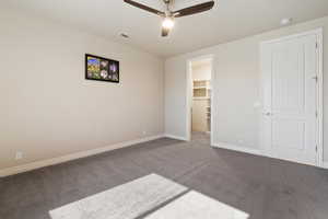 Unfurnished bedroom with a spacious closet, dark carpet, baseboards, a ceiling fan, and a closet