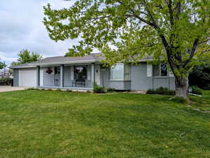 Single story home with a garage, covered porch, a front yard, driveway, and brick siding