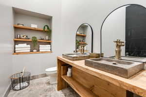 Full bathroom featuring toilet, double vanity, baseboards, and stone finish floors