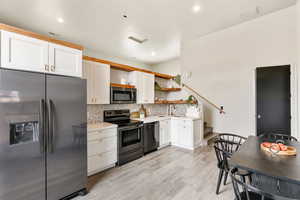 Kitchen with stainless steel appliances, open shelves, light countertops, tasteful backsplash, and white cabinetry