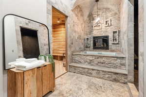 Full bathroom featuring a fireplace, a bath, and vaulted ceiling