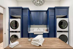 Laundry area featuring stacked washing machine and dryer, cabinet space, and a chandelier