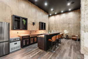 Bar featuring freestanding refrigerator, a sink, dark wood-style flooring, tasteful backsplash, and a towering ceiling