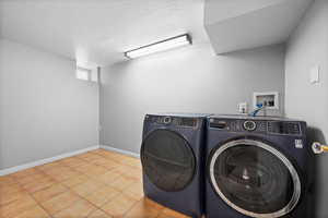 Laundry room featuring washing machine and clothes dryer, a textured ceiling, baseboards, and tile patterned floors