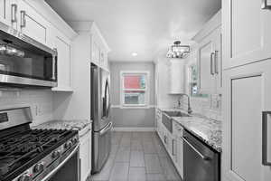 Kitchen featuring stainless steel appliances, a sink, baseboards, white cabinets, and decorative backsplash
