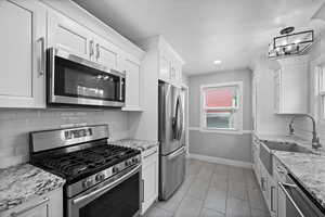 Kitchen featuring appliances with stainless steel finishes, a sink, white cabinetry, baseboards, and backsplash