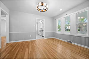 Unfurnished dining area with light wood-style flooring, a chandelier, a wainscoted wall, and baseboards