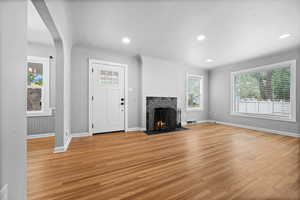 Unfurnished living room featuring light wood-style flooring, a tiled fireplace, baseboards, and recessed lighting