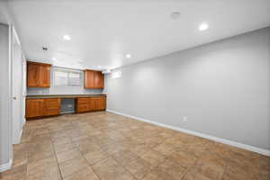 Kitchen with recessed lighting, baseboards, brown cabinetry, dark countertops, and built in desk