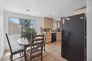 Kitchen featuring freestanding refrigerator, black dishwasher, light brown cabinets, light countertops, and healthy amount of natural light