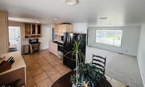 Kitchen with black fridge with ice dispenser, light tile patterned floors, light colored carpet, light countertops, and glass insert cabinets