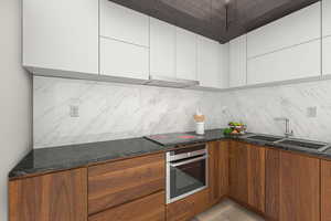 Kitchen with oven, a sink, black electric stovetop, and tasteful backsplash