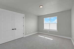Unfurnished bedroom with carpet flooring, baseboards, a textured ceiling, and a closet