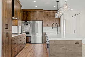 Kitchen with appliances with stainless steel finishes, a sink, a barn door, light wood-type flooring, and modern cabinets